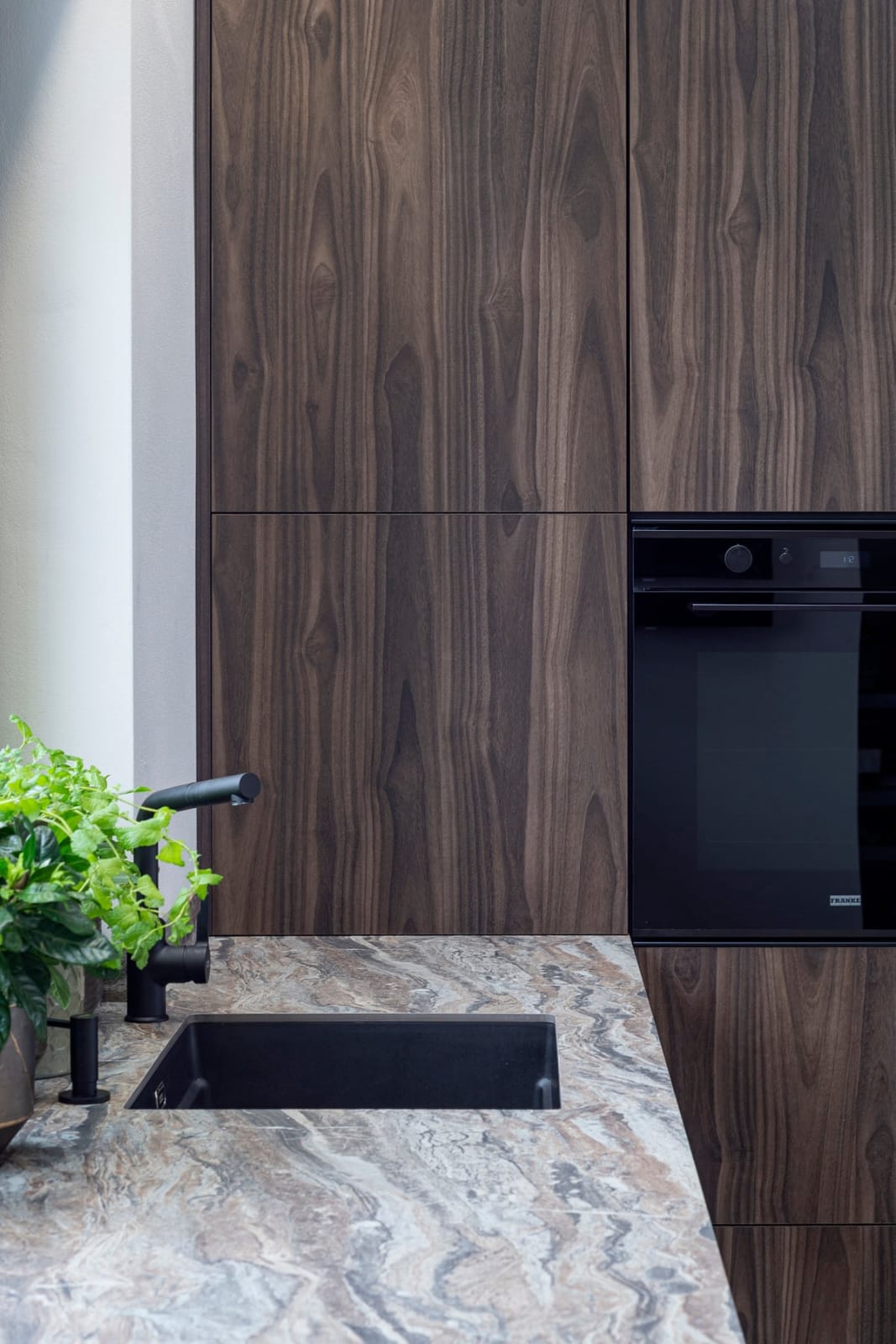 Kitchen sink zone with walnut cabinets and built-in oven