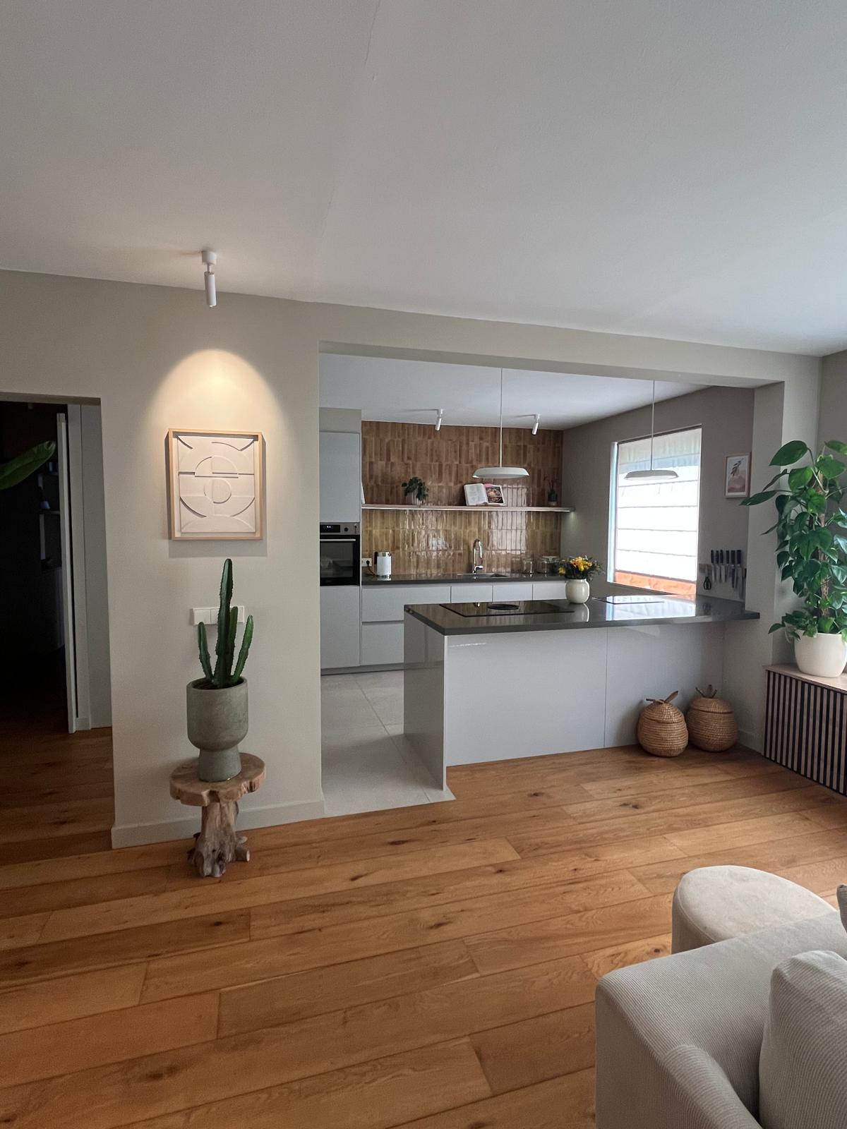 Kitchen opening into living space with oak flooring and caramel tile backsplash