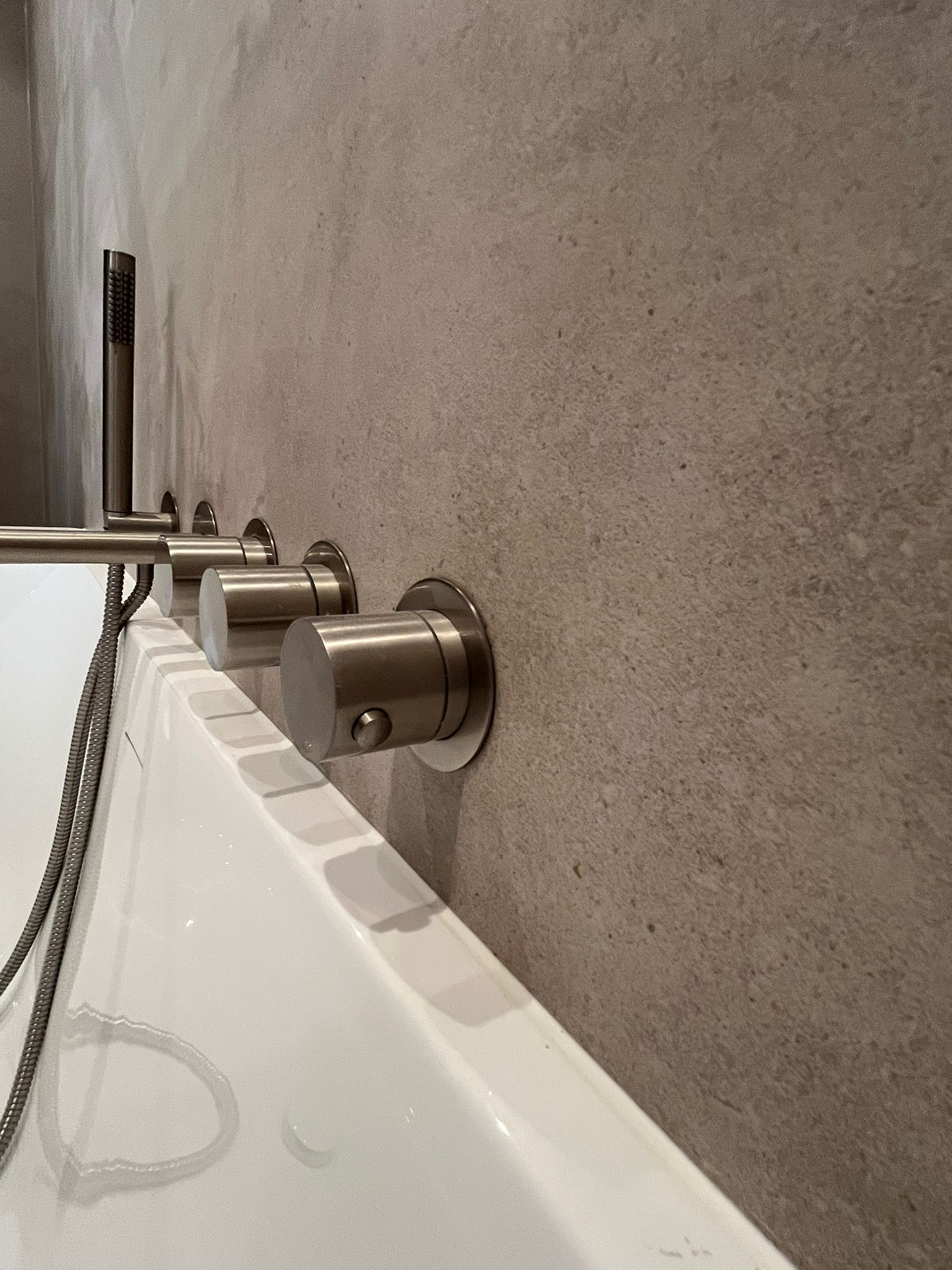 Wall-mounted brushed metal bath taps and handheld shower above white tub