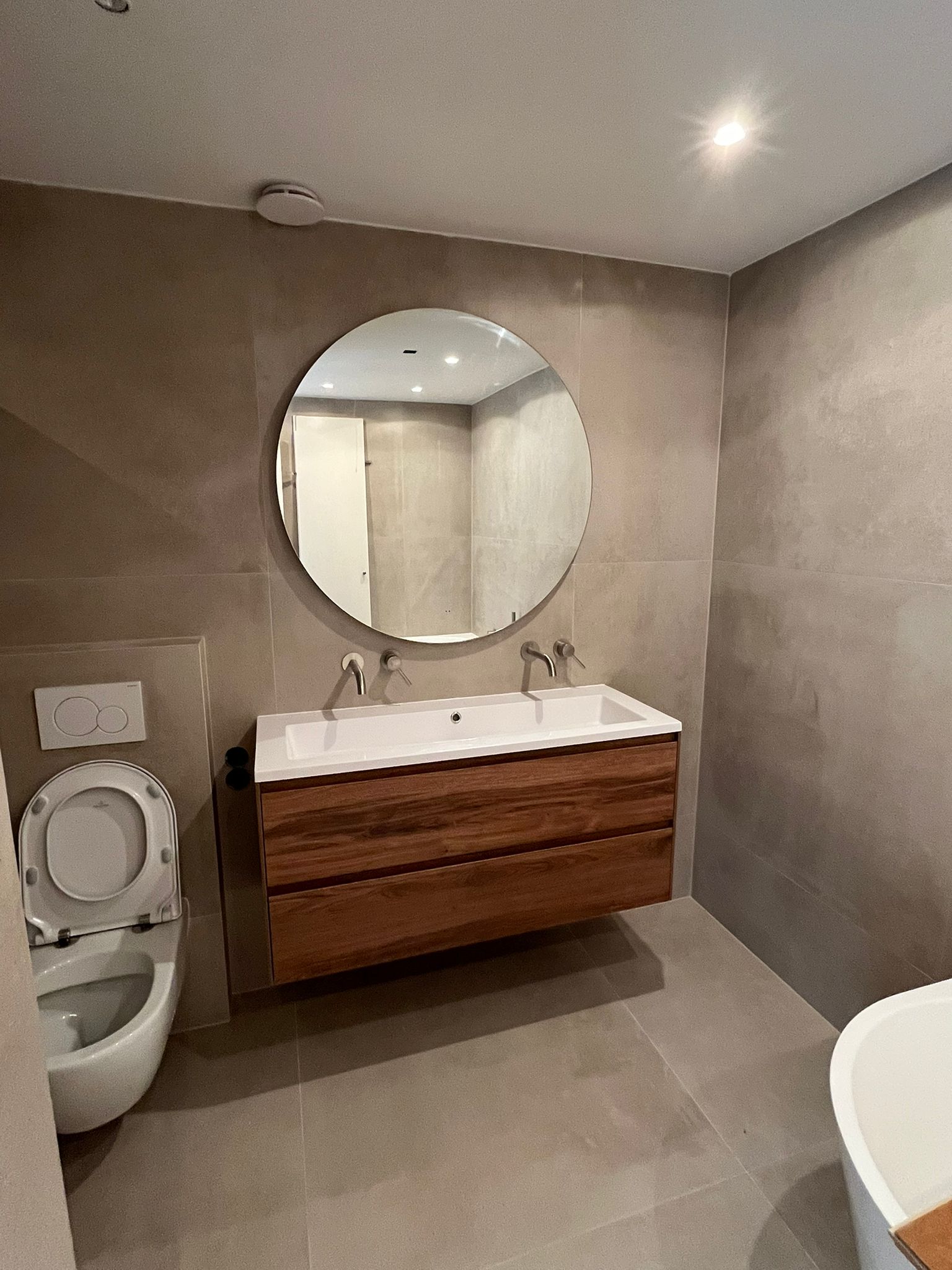 Bathroom overview with floating vanity, circular mirror and wall-hung toilet