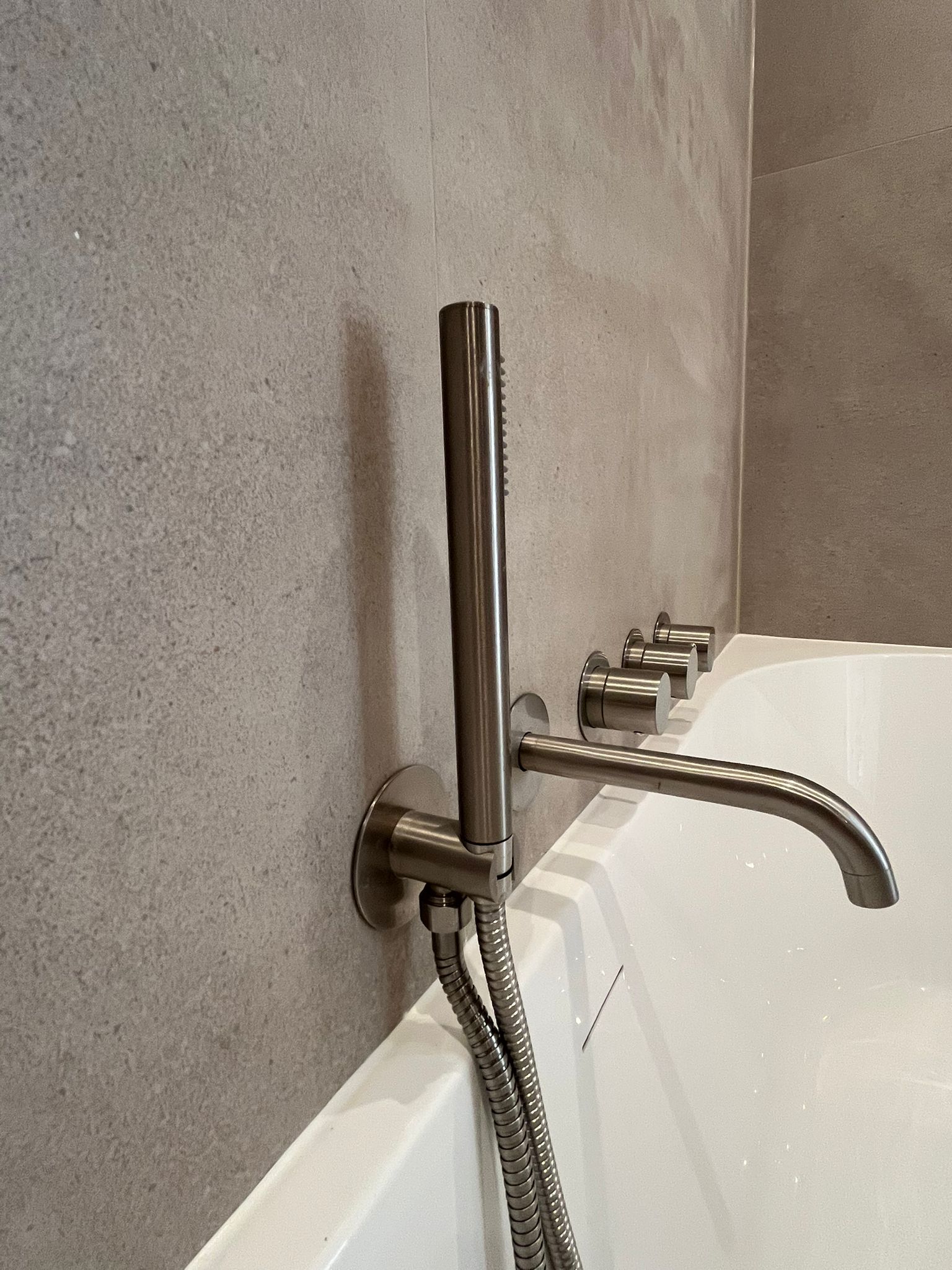 Close-up of brushed metal bath spout and shower controls on stone-effect tiles