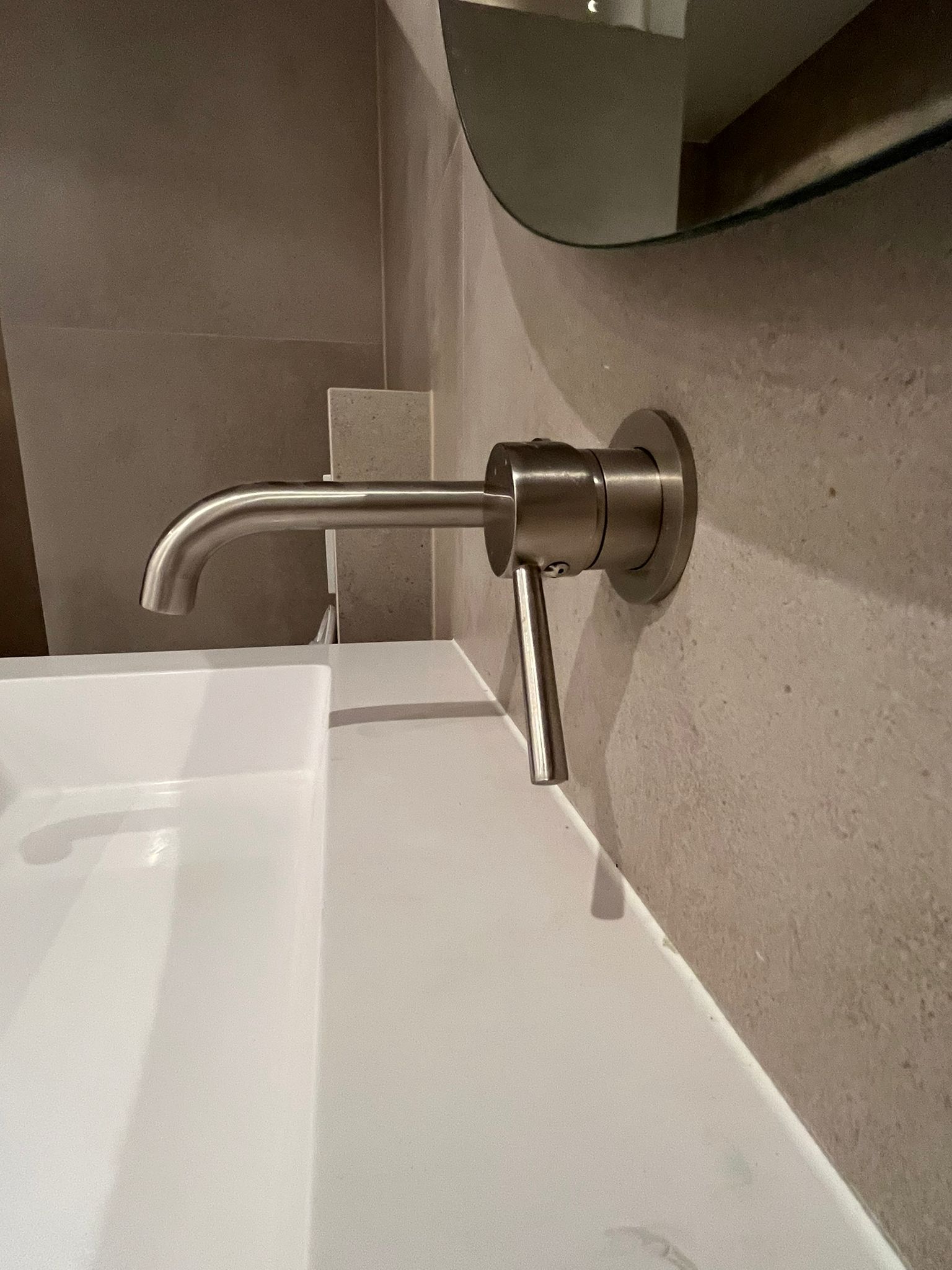 Wall-mounted brushed metal faucet above white trough basin
