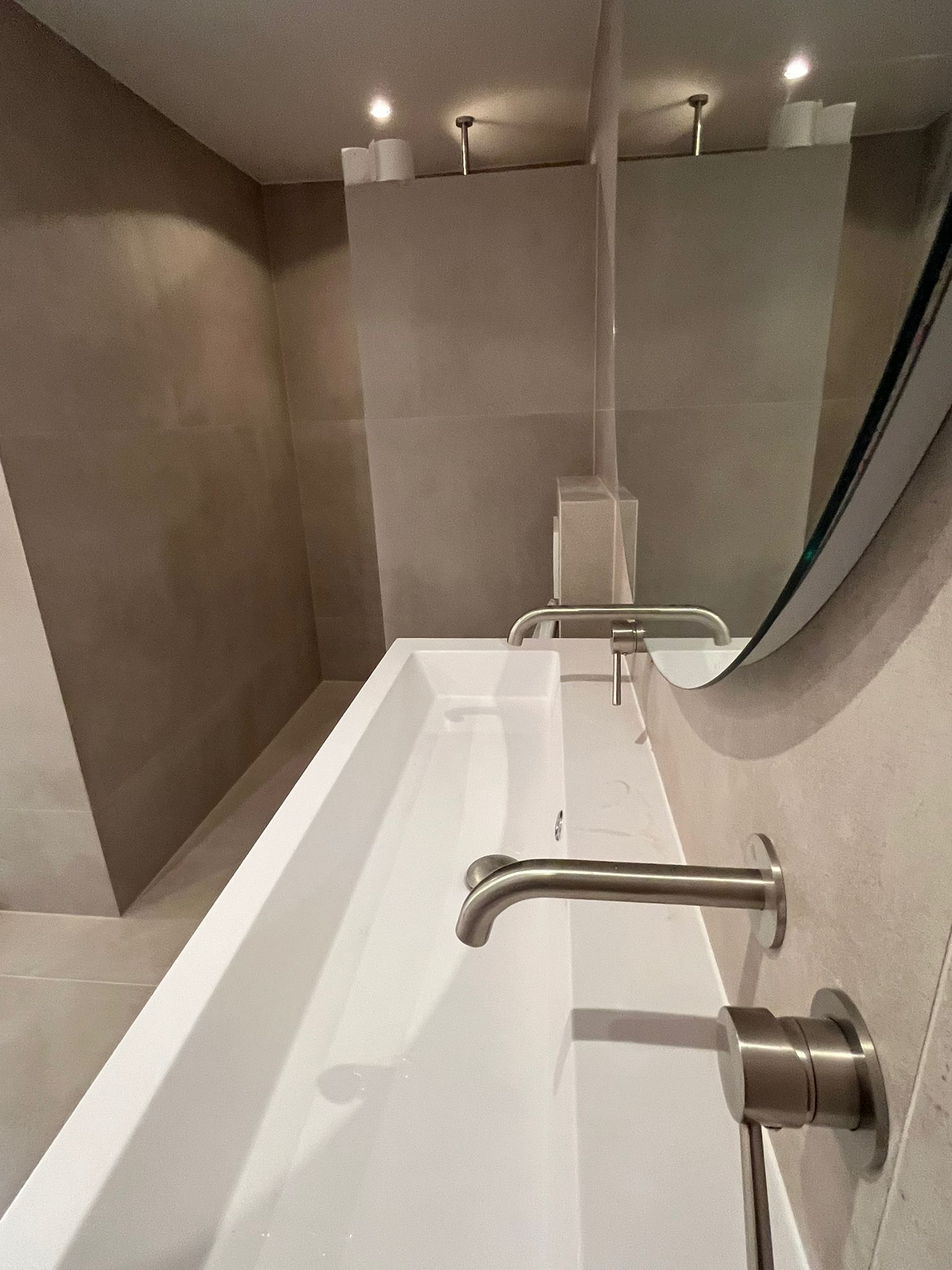 Double trough sink with twin wall-mounted faucets on matte tiled walls