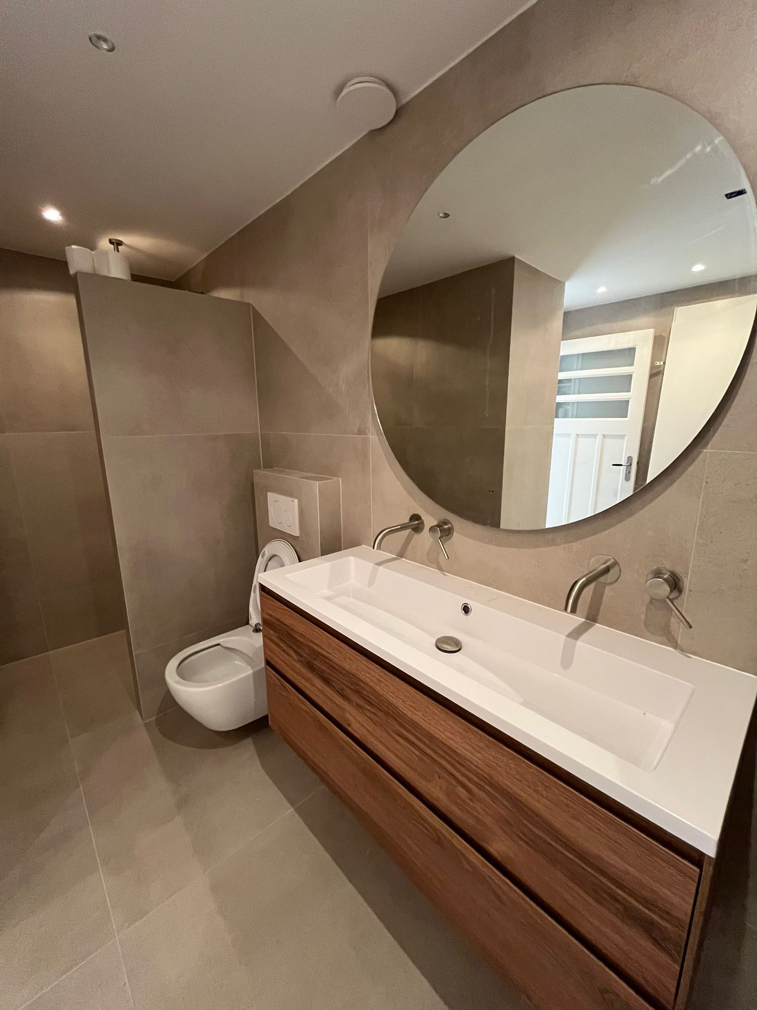 Renovated bathroom with floating walnut vanity, circular mirror and wall-hung toilet