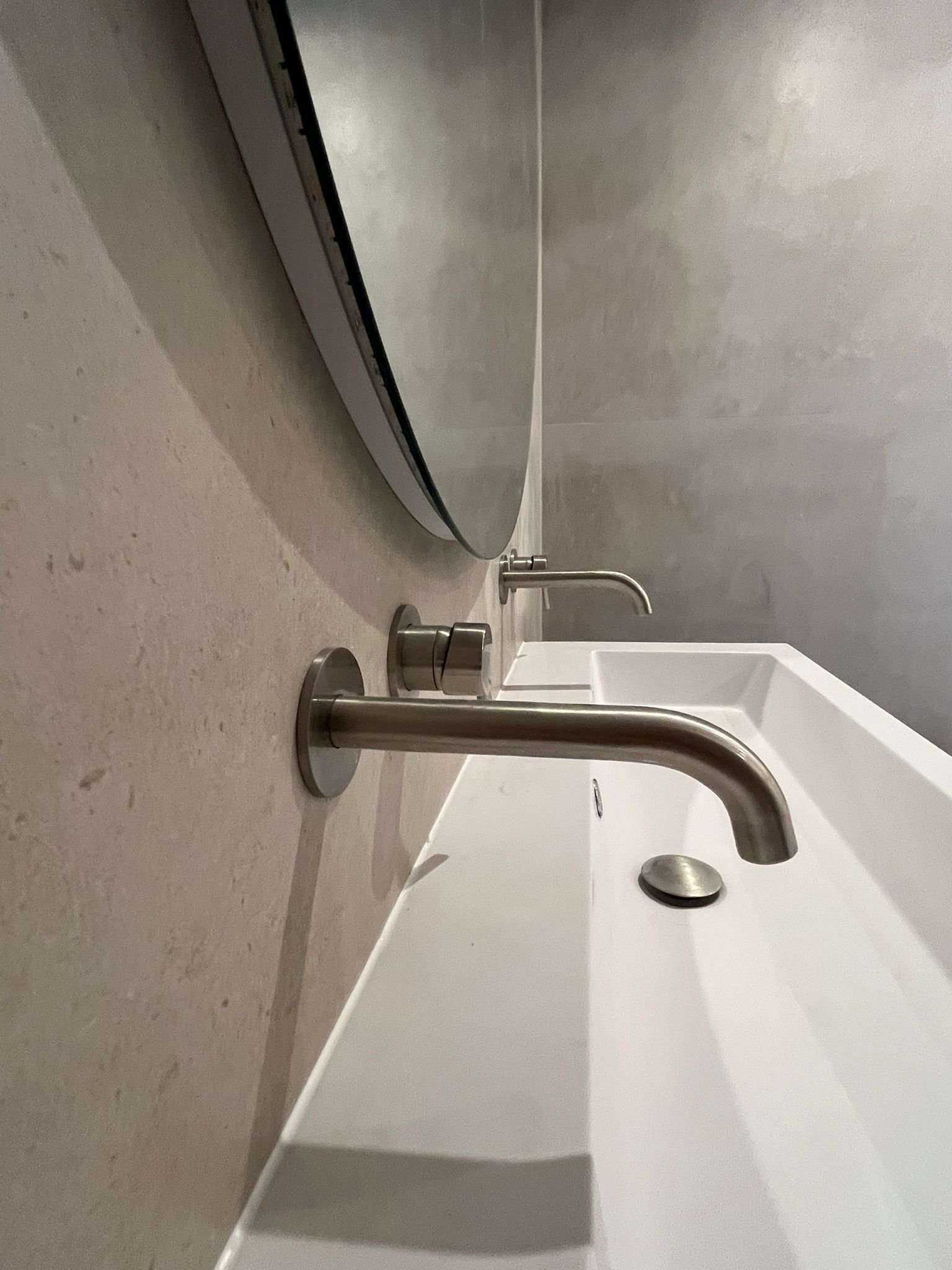 Trough sink detail with wall-mounted faucets and circular mirror