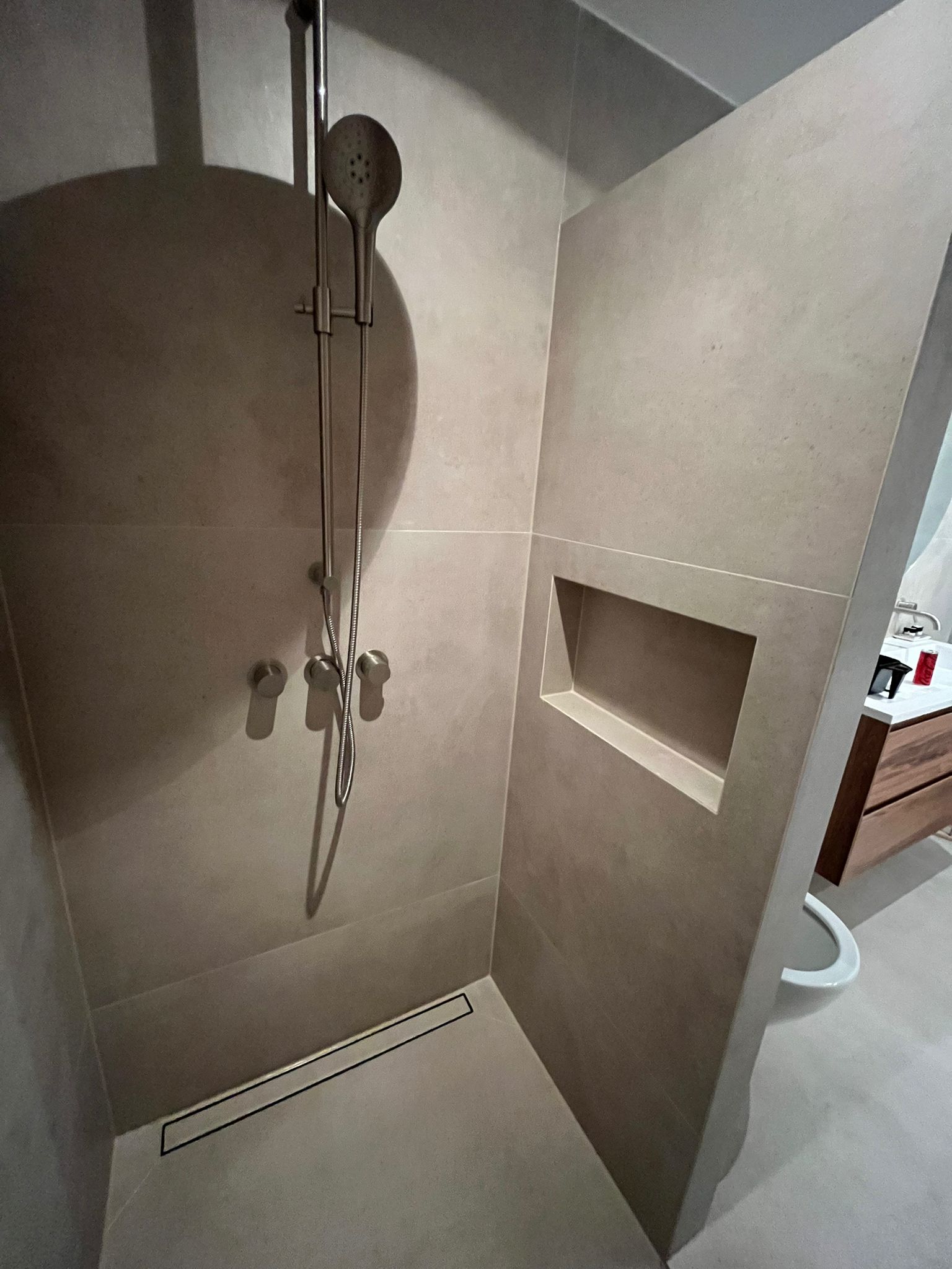 Shower area with linear drain and walnut vanity beyond