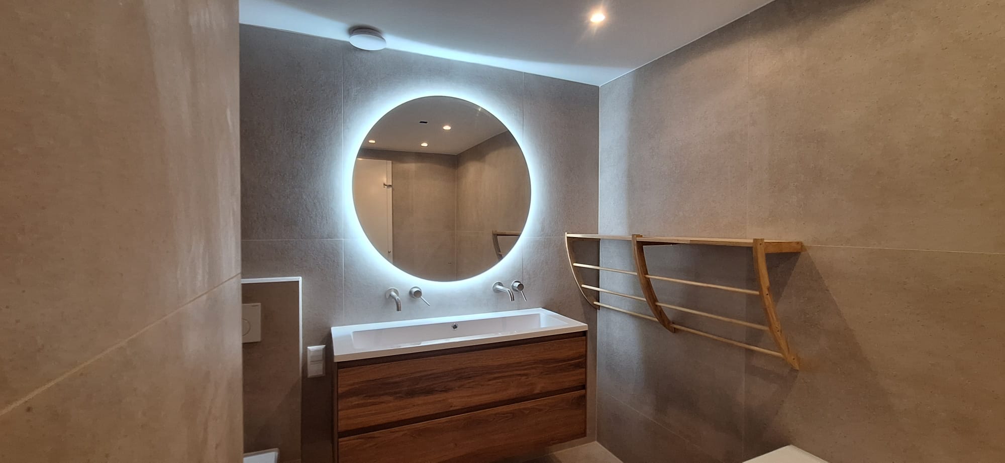 Floating walnut vanity with backlit circular mirror and wooden towel rack